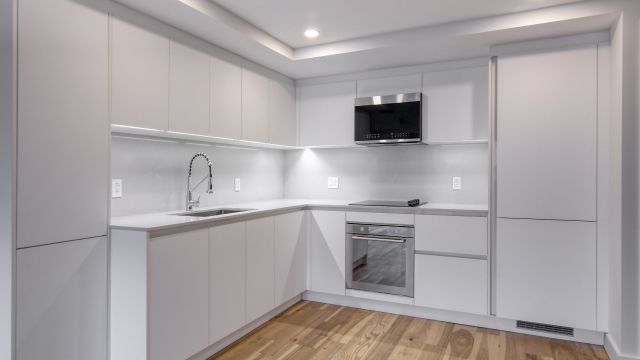 An image of an all-white kitchen featuring numerous cupboards, a sink, an oven, and a microwave positioned above the oven.