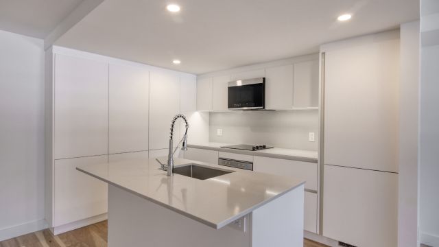 An image of a white kitchen featuring a table with a sink in the middle, surrounded by new and shiny appliances.
